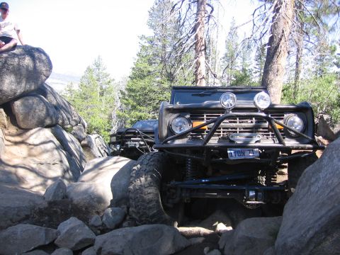 1989 Ford Bronco - A modified Ford Bronco tackles a challenging rocky terrain, with another vehicle visible behind it.