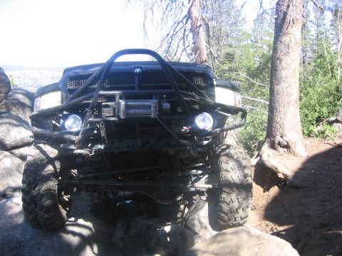 1989 Ford Bronco - This heavily modified truck navigates a rocky trail with its front end prominently displayed.