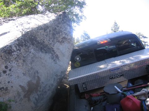 1989 Ford Bronco - A truck is stuck between a large rock and a tight space, with its bed loaded with supplies.