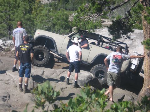 1989 Ford Bronco - A group of people stand around a white SUV parked on a dirt path surrounded by greenery.