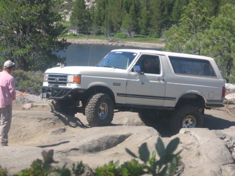 1989 Ford Bronco - A white Ford Bronco navigates a rocky path on a sunny day.