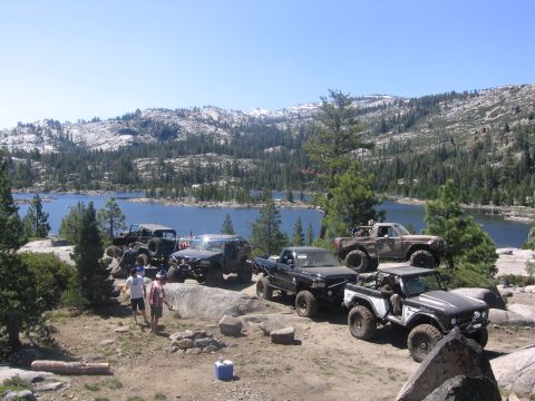 1989 Ford Bronco - A group of off-road vehicles are parked at a scenic overlook, with a lake and mountains visible in the distance.