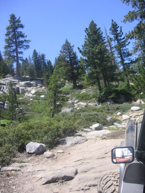 1989 Ford Bronco - An off-road vehicle navigates a rocky, wooded trail under a clear blue sky.