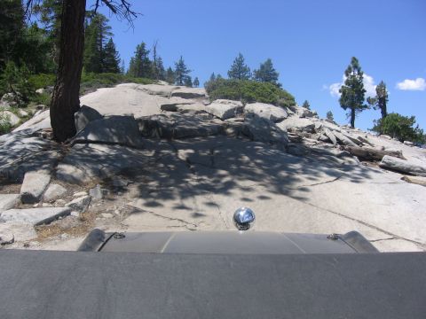 1989 Ford Bronco - View from inside a vehicle as it navigates a rocky, off-road path under a clear blue sky.