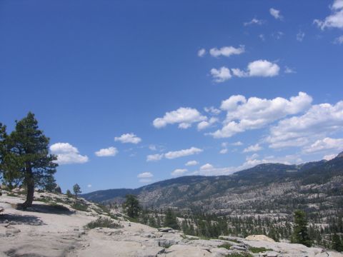 1989 Ford Bronco - Mountainous terrain with trees and a bright blue sky with white clouds.