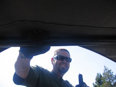 1989 Ford Bronco - A man wearing sunglasses and gloves smiles while holding onto a bar inside a vehicle, with trees visible in the background.