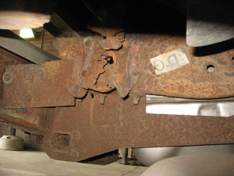 1995 Ford C-350 (Centurion Conversions) - Close-up of heavily rusted truck frame components, showing suspension attachment points and a DG sticker.