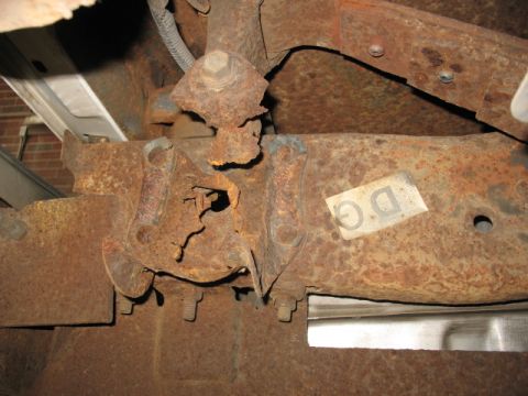 1995 Ford C-350 (Centurion Conversions) - Close-up of a heavily rusted rear spring hanger, showing significant corrosion and a label with 'DG' visible.