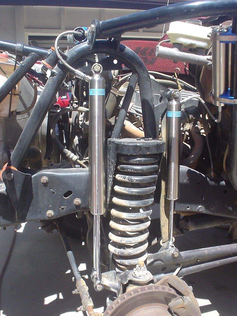 Off-road suspension with dual Bilstein shocks and large coil springs. Roll cage visible