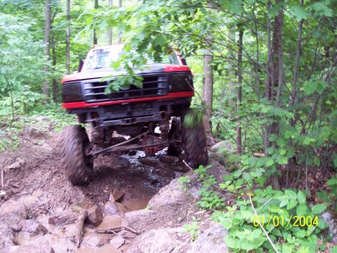 1979 Ford Bronco - This modified truck is shown tackling a challenging off-road course with significant mud and rocks.