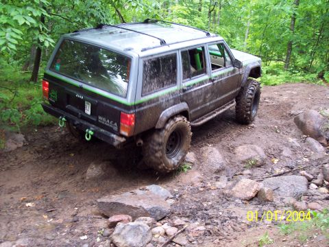 1979 Ford Bronco - A modified Jeep Cherokee XJ navigates a challenging off-road course in a wooded area.
