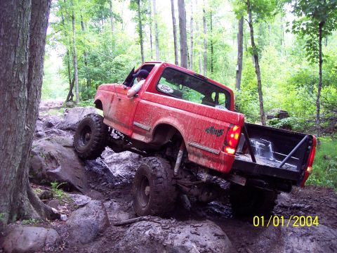 1979 Ford Bronco - Red Ford truck tackling a challenging off-road course in a wooded area.