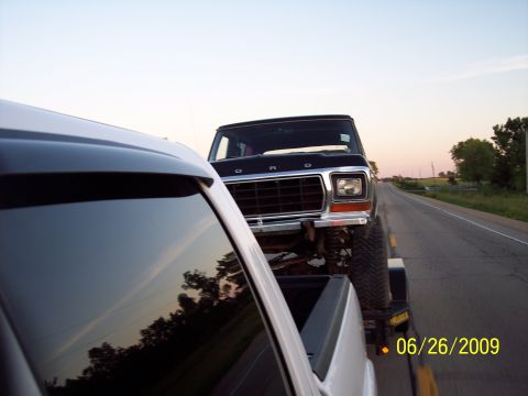 1979 Ford Bronco - A black Ford Bronco is towed on a trailer down a highway, viewed from the perspective of another vehicle.