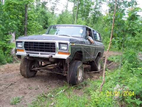 1979 Ford Bronco - A dark-colored Ford Bronco navigates a muddy, wooded trail, its off-road capabilities.