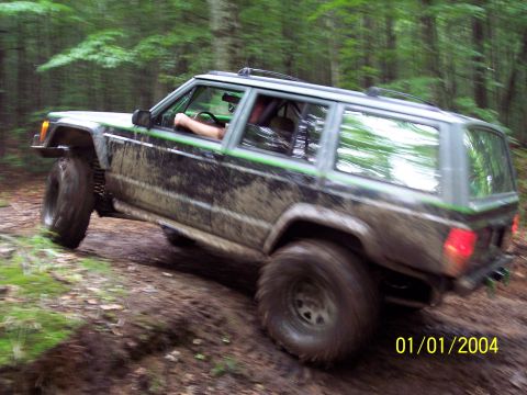 1979 Ford Bronco - A muddy Jeep Cherokee XJ navigates a challenging off-road trail through a forest.