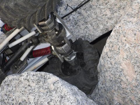 1984 Ford Bronco II - Close-up of an RC crawler's undercarriage navigating a rocky terrain.