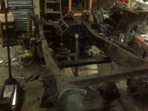1995 Ford Bronco - A disassembled vehicle chassis sits in a cluttered garage environment.