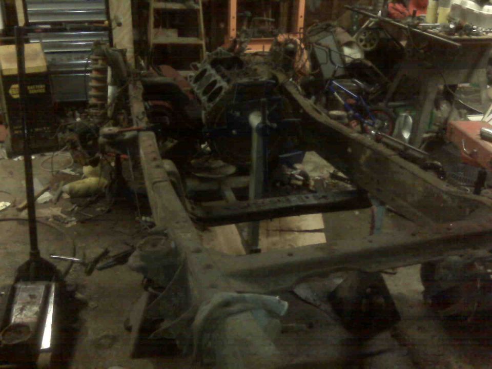 Vehicle frame and engine block in a workshop, with a floor jack visible