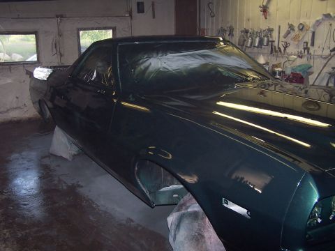 1975 Ford Ranchero - A dark green 1975 Ford Ranchero is covered in plastic sheeting, likely in a body shop for painting or repair.