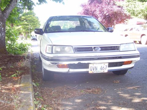 1991 Ford Bronco - White Subaru Legacy sedan parked curbside on a sunny day.