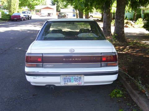 1991 Ford Bronco - This Subaru Legacy sedan is parked on a street with trees and houses. The license plate is from Oregon.