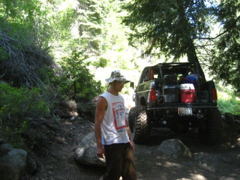 1989 Ford Bronco - A man walks past a modified black Ford Bronco on a wooded trail.