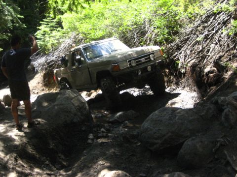 1989 Ford Bronco - A 1989 Ford Bronco tackles a challenging off-road obstacle on a wooded trail.