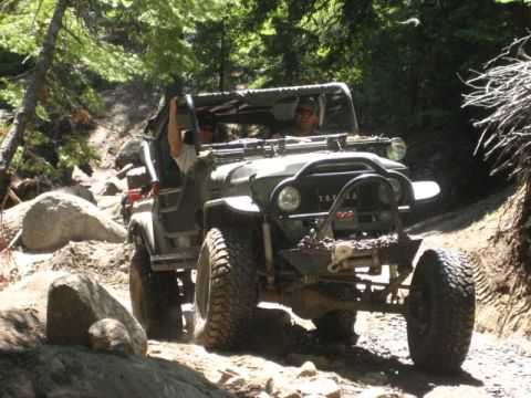 1989 Ford Bronco - This vintage Toyota Land Cruiser FJ40 navigates a challenging, rocky off-road path surrounded by trees.