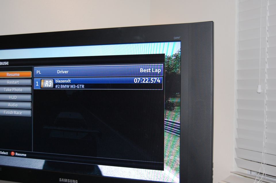 Television screen displaying a racing game pause menu with driver names and lap times