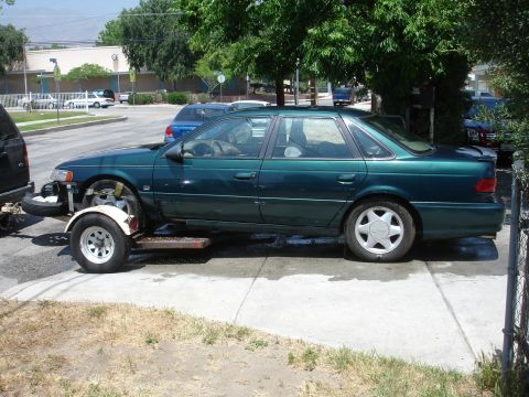 1995 Ford Taurus - Green 1995 Ford Taurus being transported on a trailer with its front bumper missing.