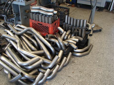 1992 Ford Taurus - A large collection of exhaust pipes are organized in crates and piled on the floor of a workshop.