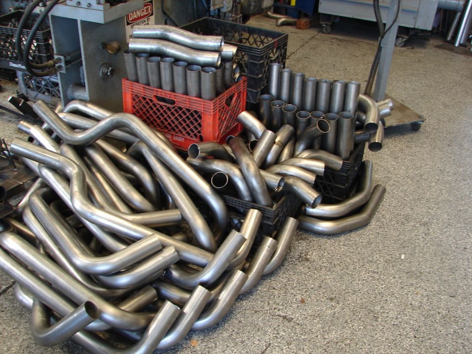 Pile of bent metal exhaust pipes in a workshop, some in red and black crates