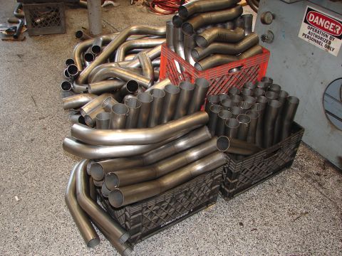 1992 Ford Taurus - A large collection of metal exhaust pipes are organized in plastic crates within a workshop environment.