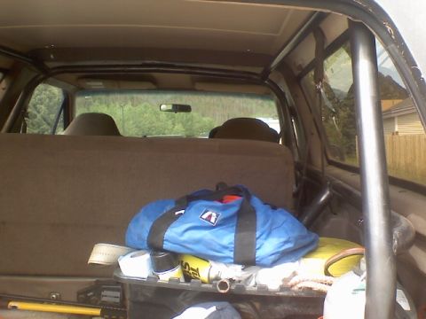 1993 Ford Bronco - View into the cargo area of a Ford Bronco through the open rear hatch, showing a bare-steel roll bar tube running down the rear corner and…