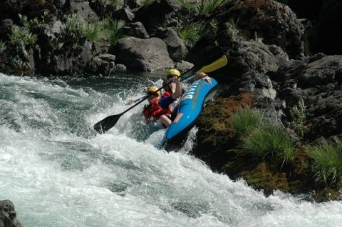 1994 Ford Bronco - Two individuals navigate a challenging whitewater rapid in a blue raft, surrounded by rocky terrain and lush vegetation.