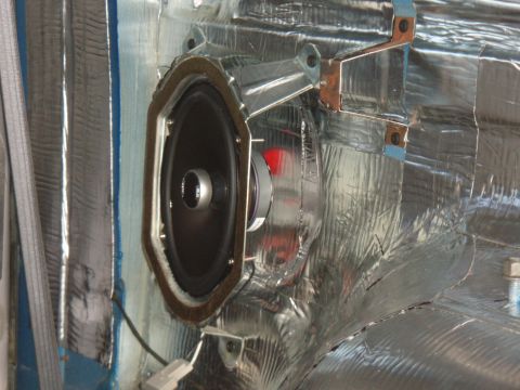 1996 Ford Bronco - A car speaker is installed in a door panel, covered with sound-deadening material.