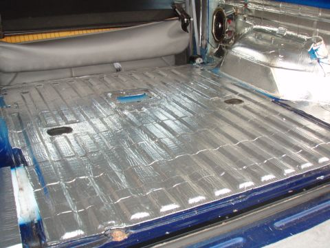 1996 Ford Bronco - The interior cargo area of a vehicle is covered in silver sound deadening material, with a speaker visible in the upper right corner.