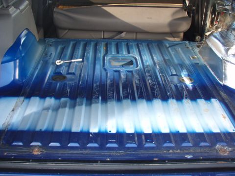 1996 Ford Bronco - The interior cargo area of a vehicle shows a blue painted floor with some scuff marks and a ratchet.