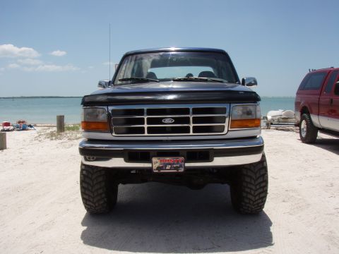 1996 Ford Bronco - A black Ford Bronco is parked on a beach with the ocean in the background.