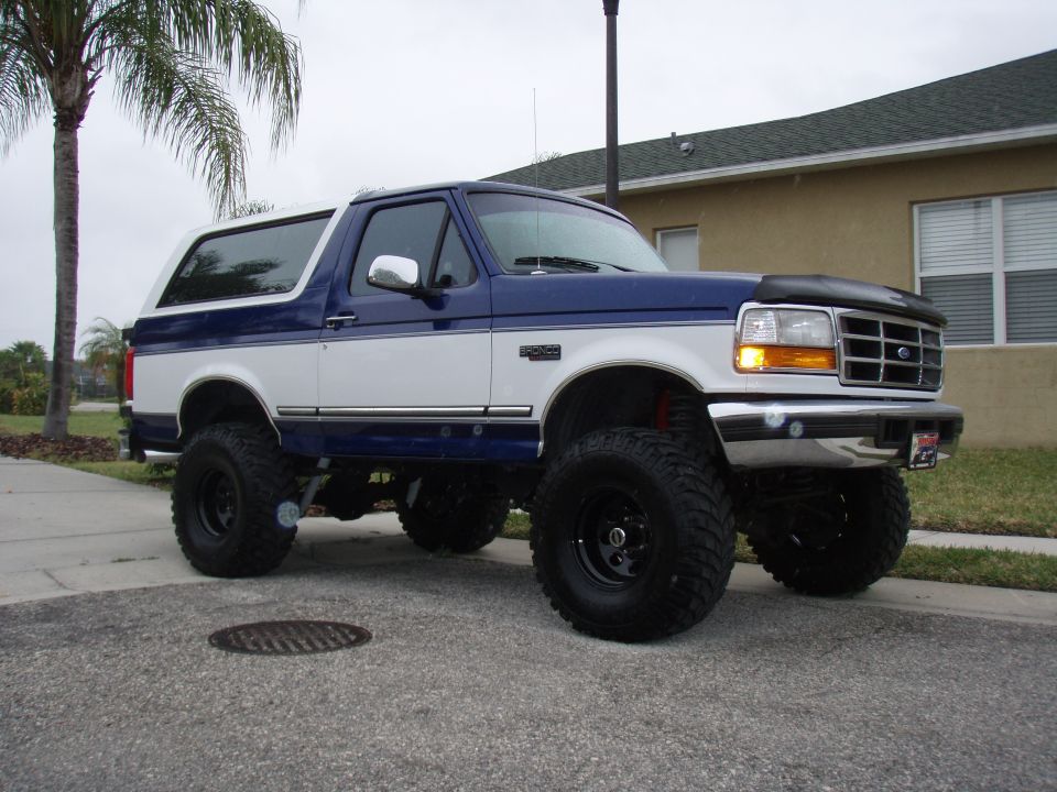 Blue and white lifted Ford Bronco with large tires parked on a street