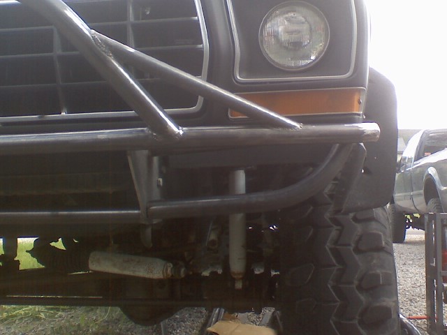 1978 Ford Bronco front end with custom roll cage and off-road tires. Another pickup truck is visible in the background