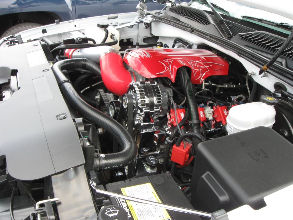 Engine bay with red intake hose and red engine covers with white pinstriping. Chrome alternator and red ignition coils are visible