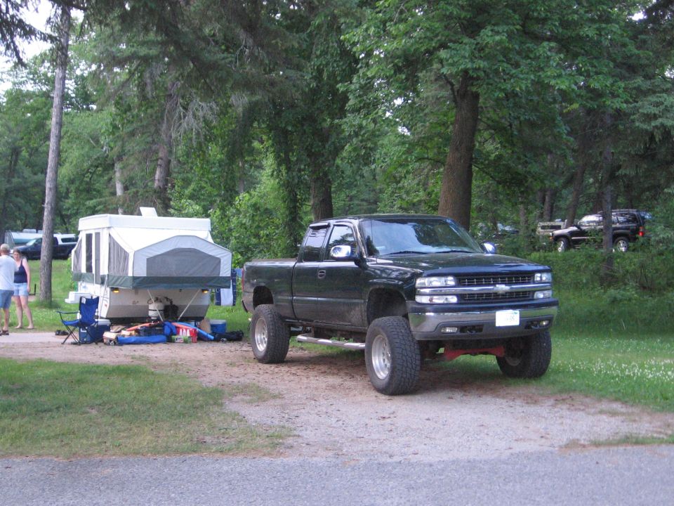 Lifted dark Chevrolet Silverado pickup towing a pop-up camper