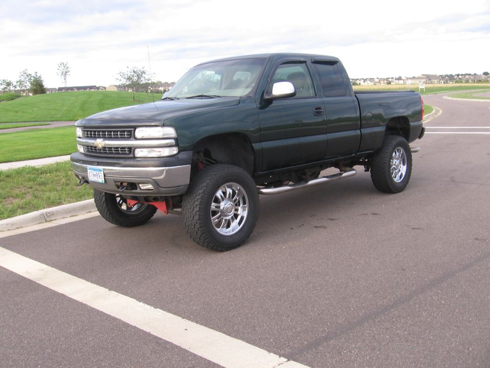 Dark green 2001 Chevrolet Silverado 1500 pickup truck with chrome wheels and running boards, lifted suspension, parked on asphalt