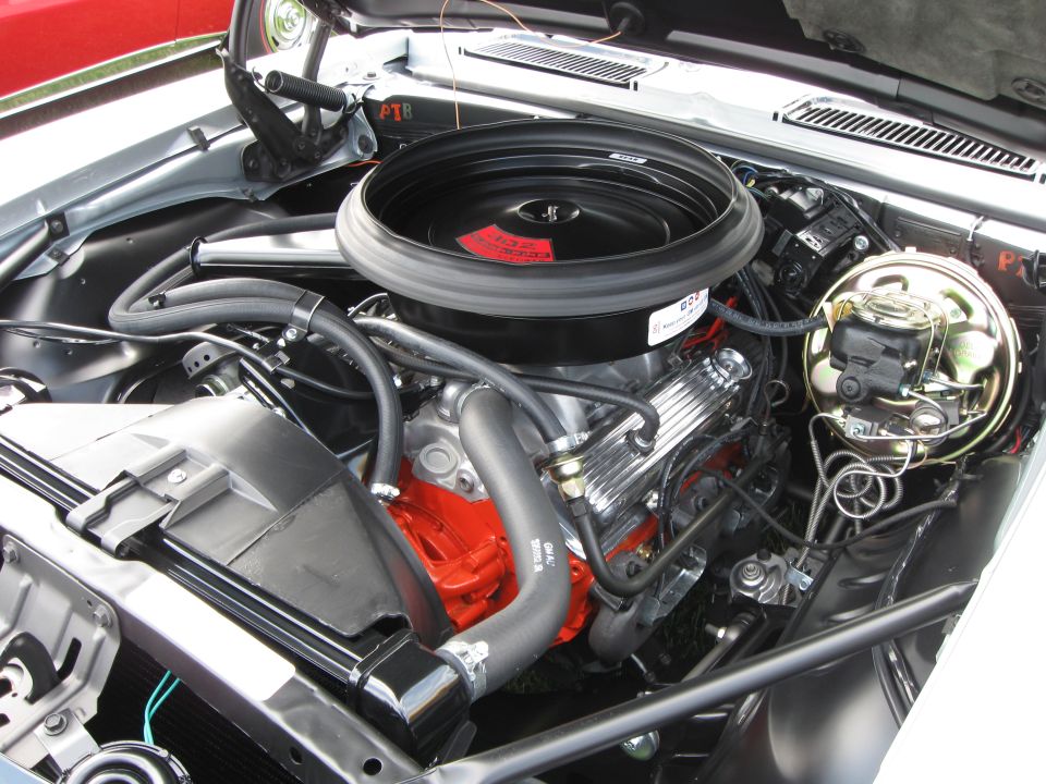 Engine bay with V8 engine, chrome valve covers, large black air cleaner, and red engine block. Silver car exterior visible