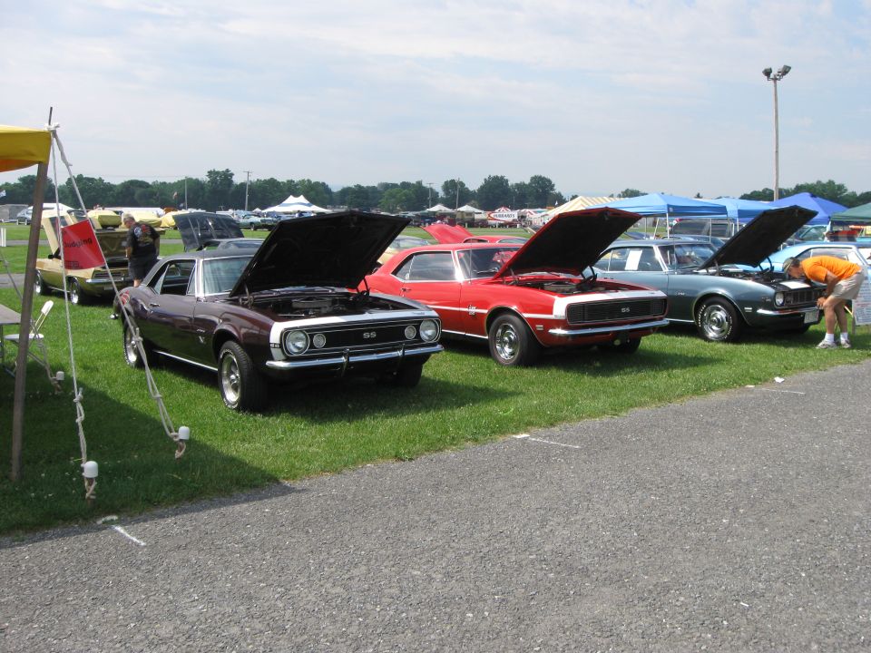 Dark purple 1969 Camaro SS with hood open, parked next to red and green Camaros