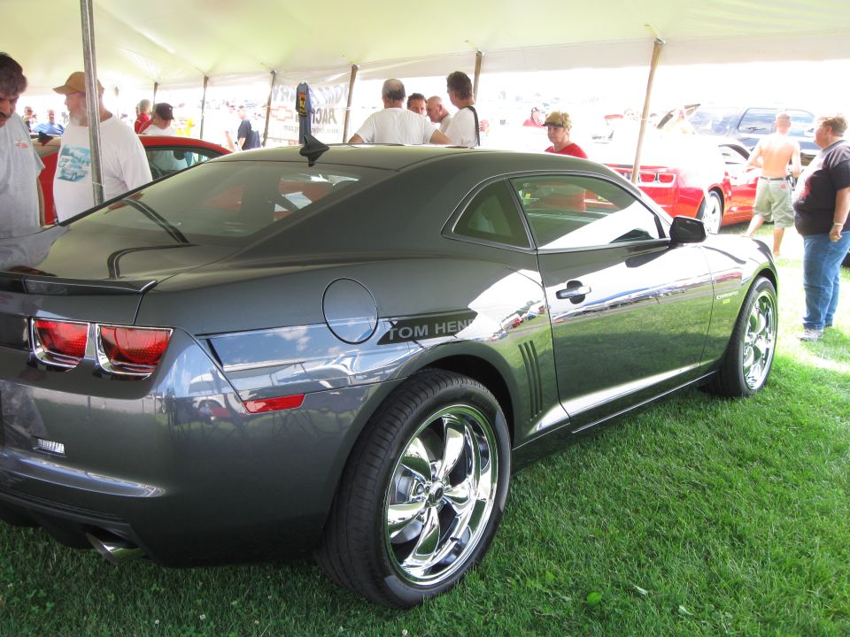 Dark gray coupe with chrome wheels and "TOM HENRY" text on the side, parked on grass under a tent