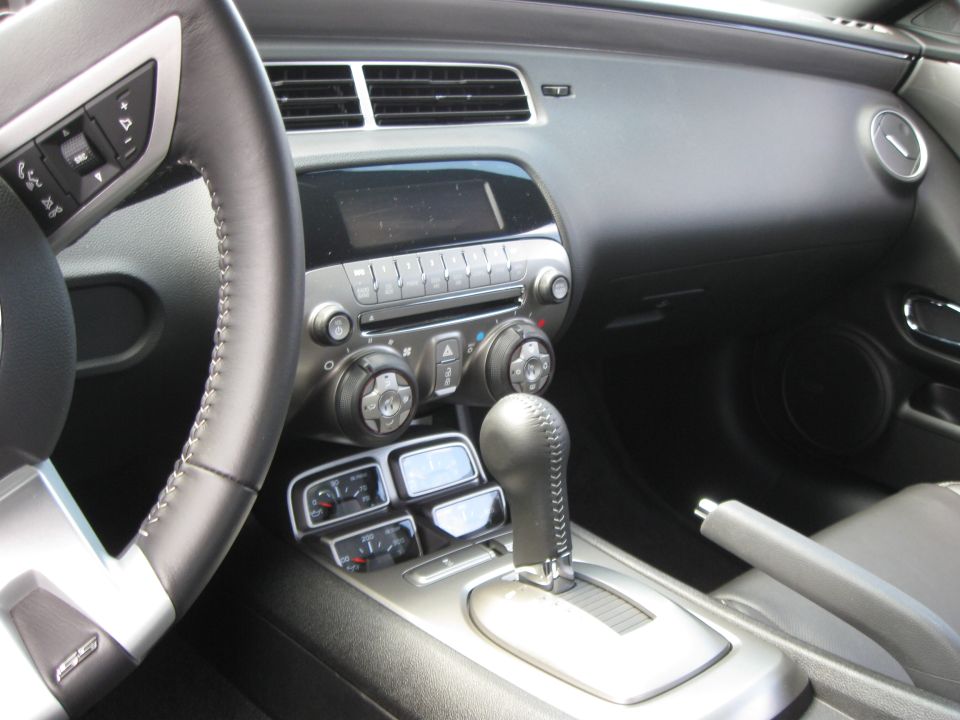 Car interior with leather-wrapped steering wheel, dashboard, center console with automatic shifter, and auxiliary gauges