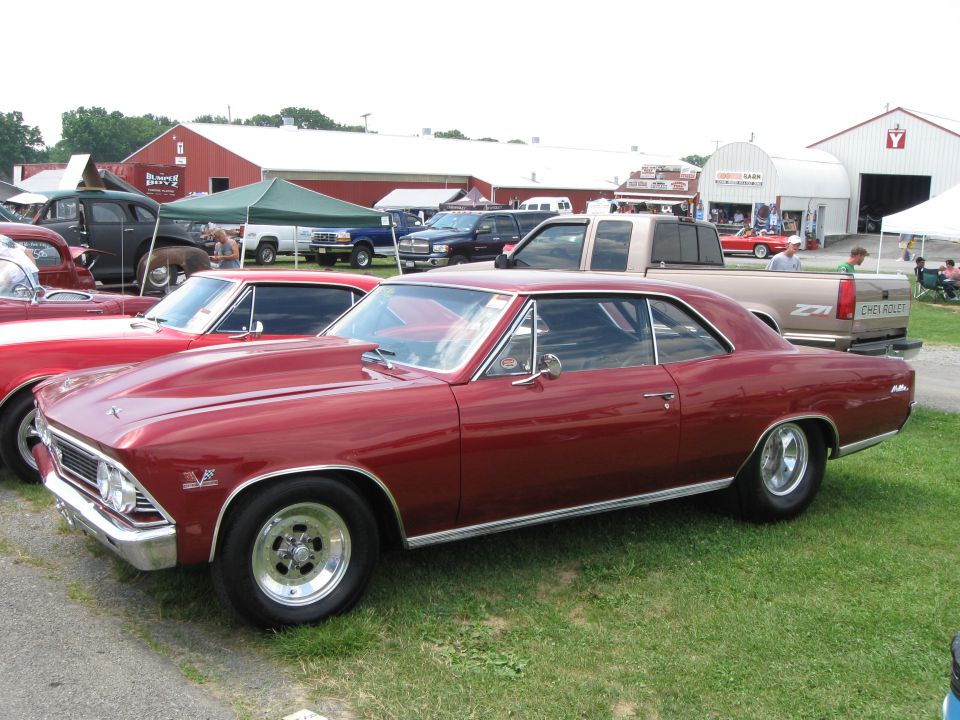 Red 1966 Chevelle SS with a cowl induction hood parked on grass next to other cars and trucks