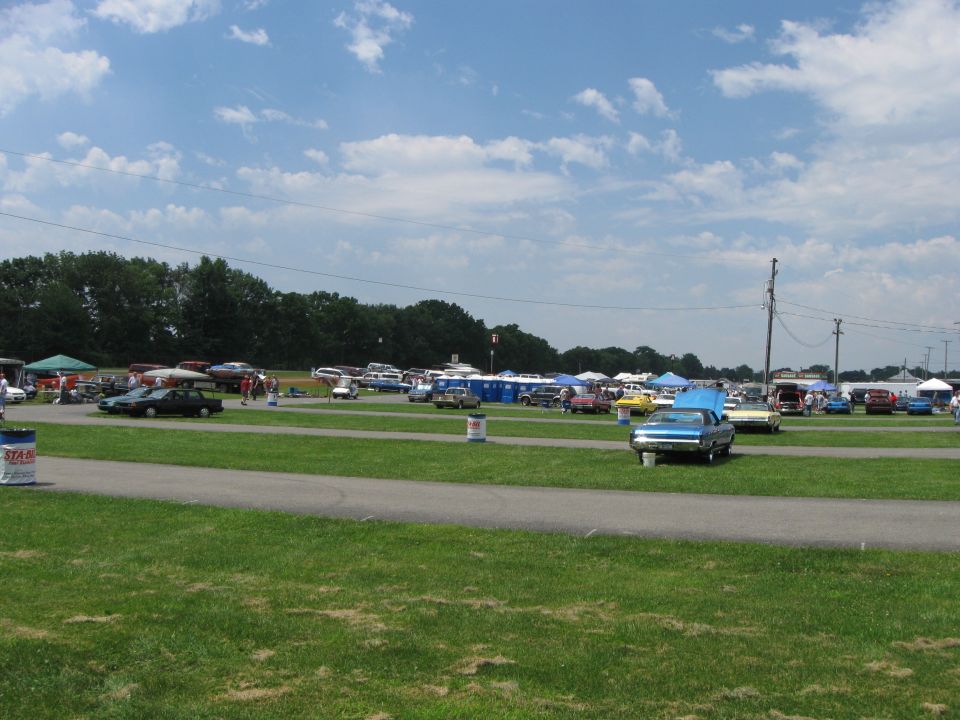 Blue car with hood open parked on grass at an outdoor event with many other vehicles